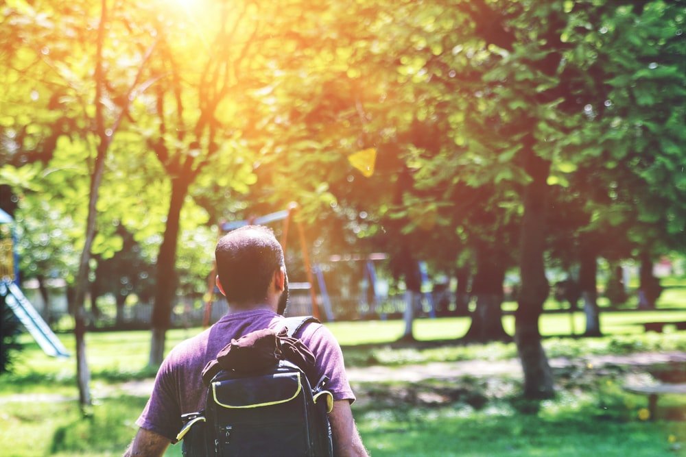 man in black t-shirt with black backpack walking near trees